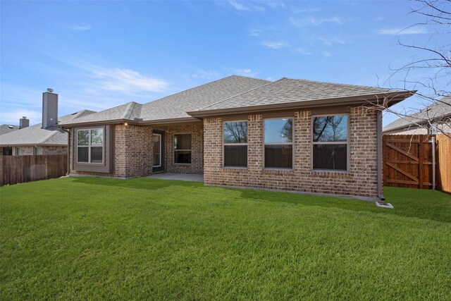 back of property with a lawn, a fenced backyard, brick siding, and a shingled roof