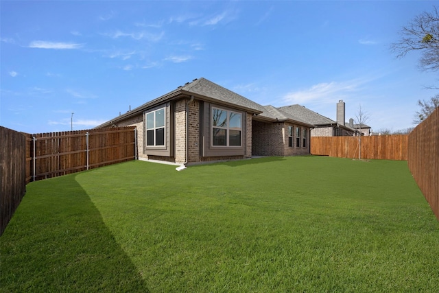 back of house with brick siding, a fenced backyard, a shingled roof, and a yard