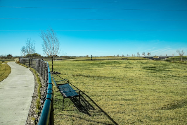 view of community featuring a rural view, fence, and a lawn