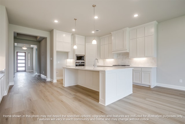 kitchen with light countertops, a kitchen island with sink, white cabinetry, built in microwave, and oven