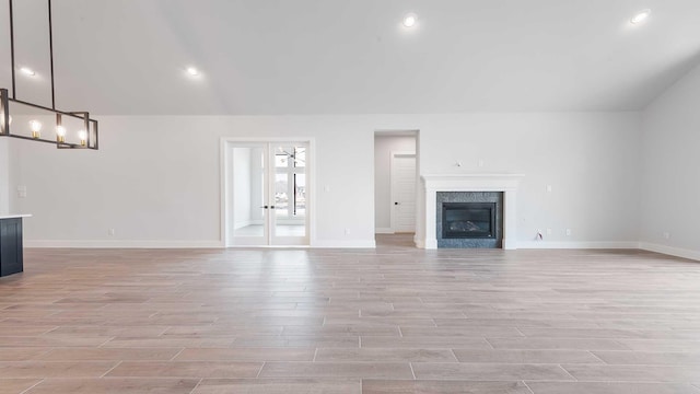 unfurnished living room with lofted ceiling, a fireplace, baseboards, and light wood finished floors