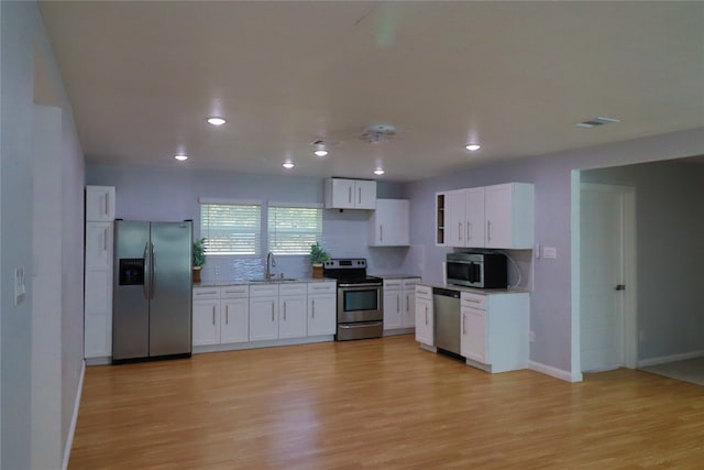 kitchen with backsplash, sink, appliances with stainless steel finishes, white cabinets, and light hardwood / wood-style floors