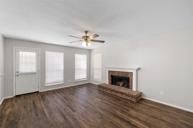 unfurnished living room with a textured ceiling, dark wood-type flooring, ceiling fan, and a brick fireplace