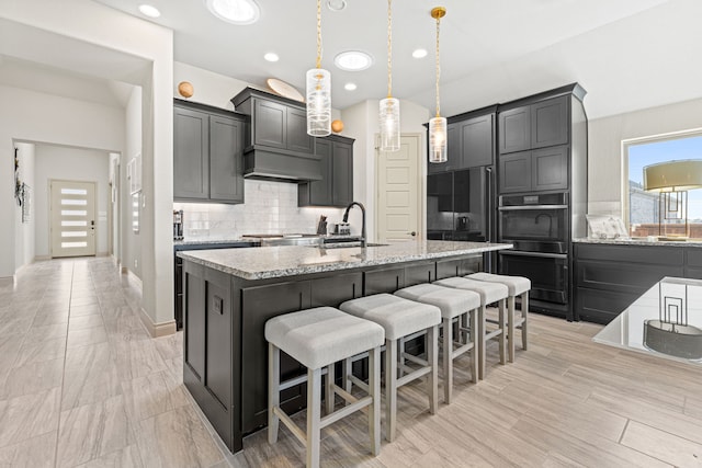 kitchen with light stone countertops, tasteful backsplash, an island with sink, a kitchen bar, and sink