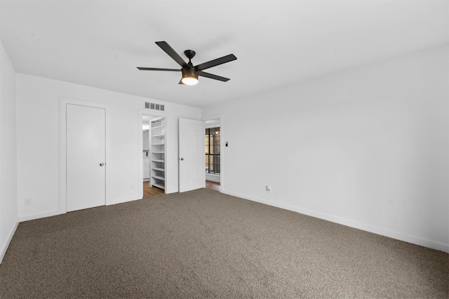 unfurnished bedroom featuring a closet, a walk in closet, ceiling fan, and carpet floors