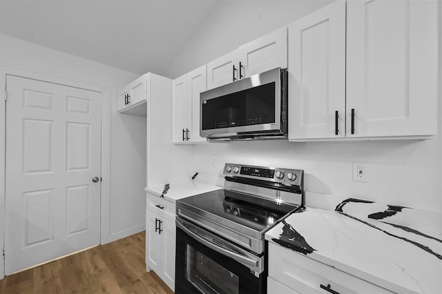 kitchen with light stone counters, dark wood-type flooring, appliances with stainless steel finishes, lofted ceiling, and white cabinets