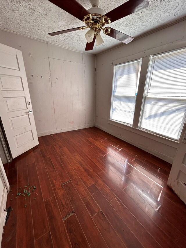 interior space featuring dark wood-type flooring, ceiling fan, wooden walls, and a textured ceiling