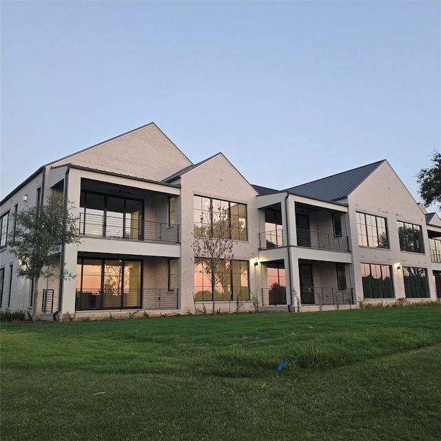 rear view of property featuring a balcony, a lawn, and stucco siding