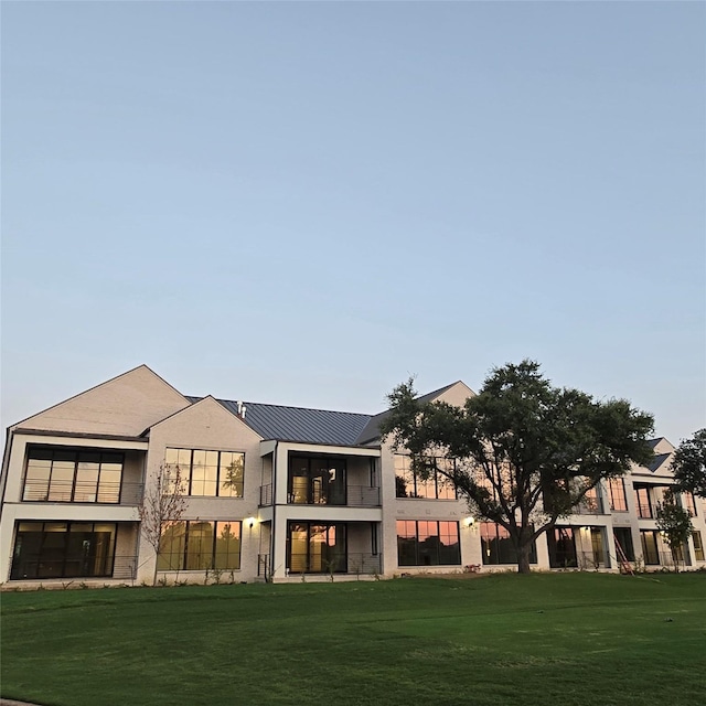 back of property with metal roof, a yard, a balcony, and stucco siding