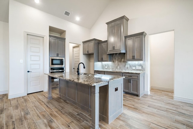 kitchen with sink, light hardwood / wood-style flooring, an island with sink, light stone counters, and stainless steel appliances