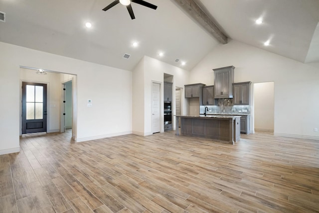 kitchen with beam ceiling, ceiling fan, sink, light hardwood / wood-style flooring, and an island with sink