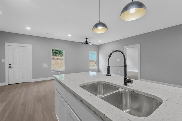 kitchen featuring pendant lighting, light hardwood / wood-style flooring, light stone counters, sink, and ceiling fan