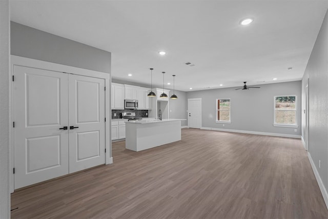 kitchen featuring pendant lighting, appliances with stainless steel finishes, a kitchen island with sink, light wood-type flooring, and white cabinets