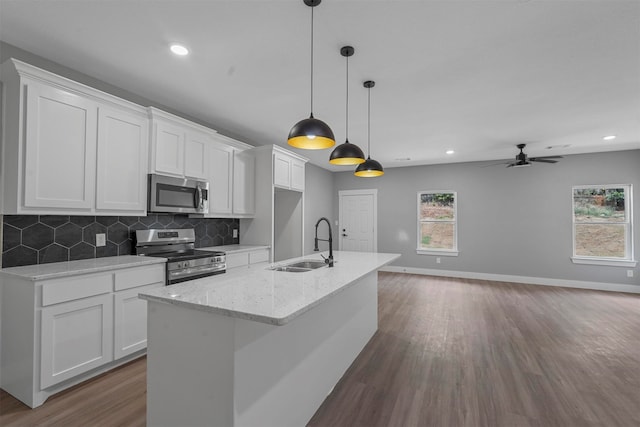 kitchen featuring a kitchen island with sink, white cabinetry, stainless steel appliances, light stone counters, and ceiling fan