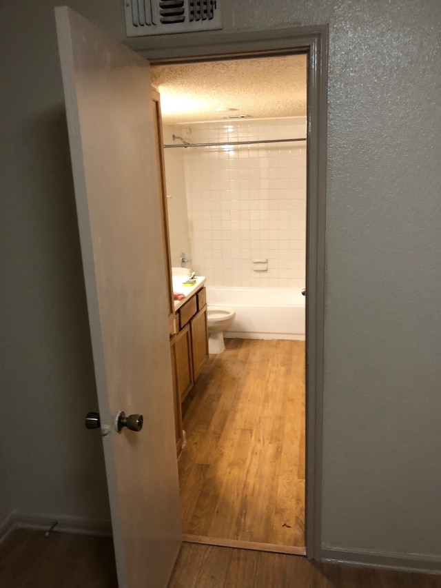 full bathroom with a textured ceiling, vanity, wood-type flooring, toilet, and tiled shower / bath combo