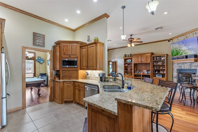 kitchen featuring billiards, light hardwood / wood-style flooring, appliances with stainless steel finishes, a stone fireplace, and ceiling fan