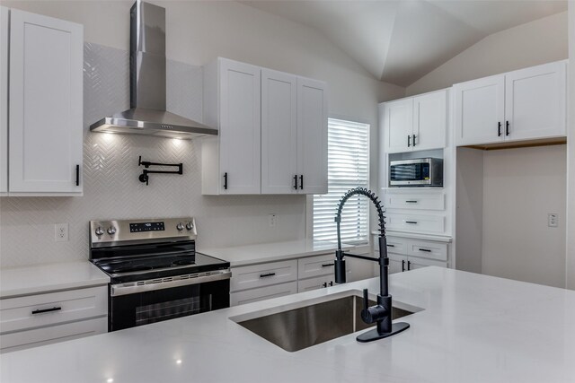 kitchen featuring lofted ceiling, white cabinets, stainless steel appliances, and wall chimney exhaust hood