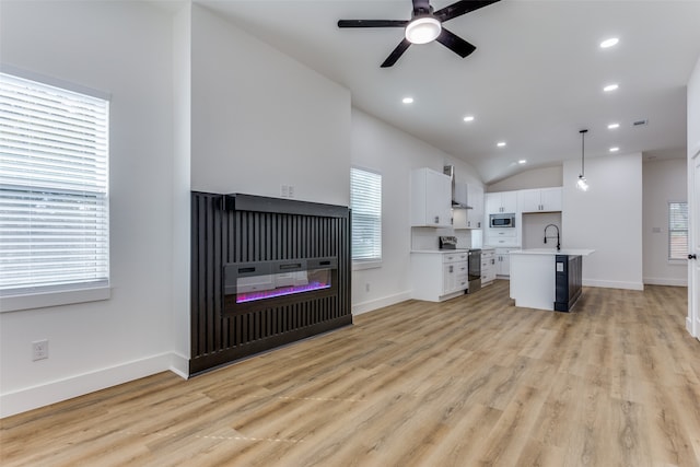 living room with ceiling fan, sink, light wood-type flooring, and vaulted ceiling