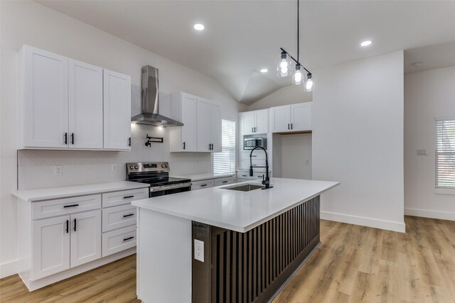 kitchen with vaulted ceiling, appliances with stainless steel finishes, sink, wall chimney exhaust hood, and a kitchen island with sink