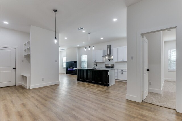 kitchen with a kitchen island with sink, hanging light fixtures, wall chimney range hood, white cabinets, and stainless steel range with electric cooktop