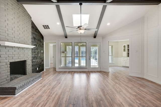 unfurnished living room featuring vaulted ceiling with beams, ceiling fan, wood-type flooring, and a brick fireplace