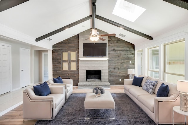 living room with dark wood-type flooring, ceiling fan, wooden walls, vaulted ceiling with skylight, and a brick fireplace