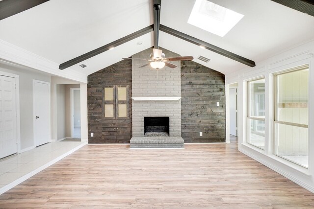 unfurnished living room with a brick fireplace, light wood-type flooring, lofted ceiling with skylight, a ceiling fan, and visible vents