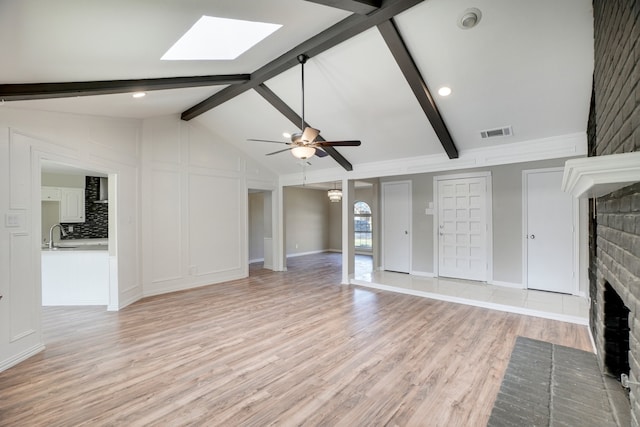 unfurnished living room with ceiling fan, sink, a brick fireplace, light hardwood / wood-style flooring, and vaulted ceiling with skylight