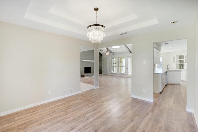 unfurnished living room featuring sink, a brick fireplace, a raised ceiling, ceiling fan, and light hardwood / wood-style floors