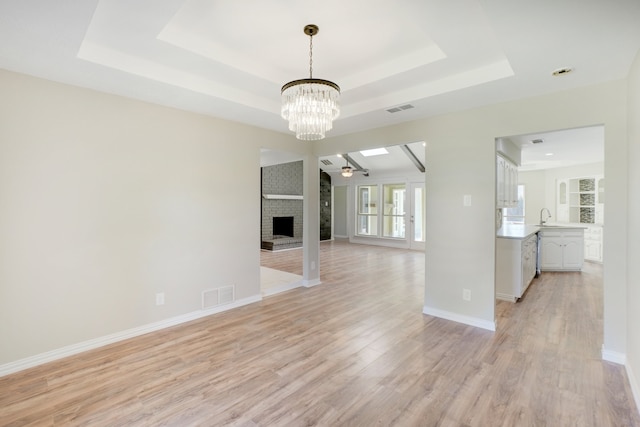 unfurnished living room featuring a fireplace, a raised ceiling, ceiling fan with notable chandelier, and light hardwood / wood-style flooring