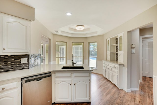 kitchen with kitchen peninsula, white cabinetry, sink, stainless steel dishwasher, and a tray ceiling