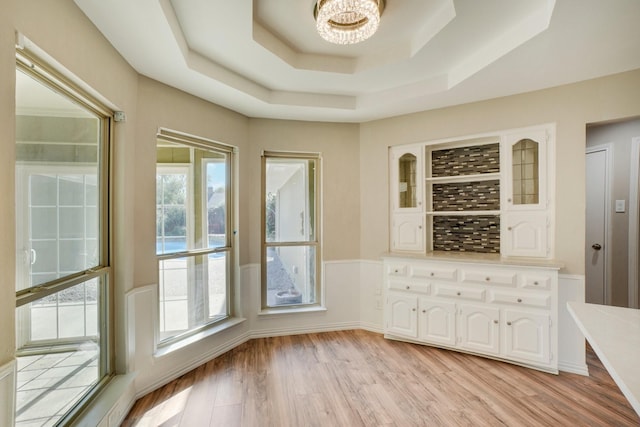 interior space with a notable chandelier, light hardwood / wood-style flooring, and a raised ceiling