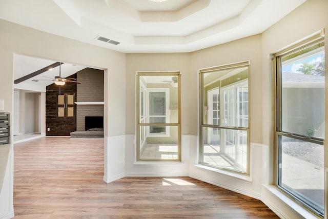 interior space with a raised ceiling, ceiling fan, and light hardwood / wood-style floors