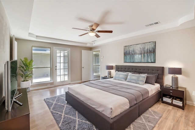 bedroom with a tray ceiling, access to outside, ceiling fan, and light wood-type flooring