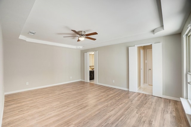 empty room featuring a tray ceiling, light hardwood / wood-style floors, and ceiling fan