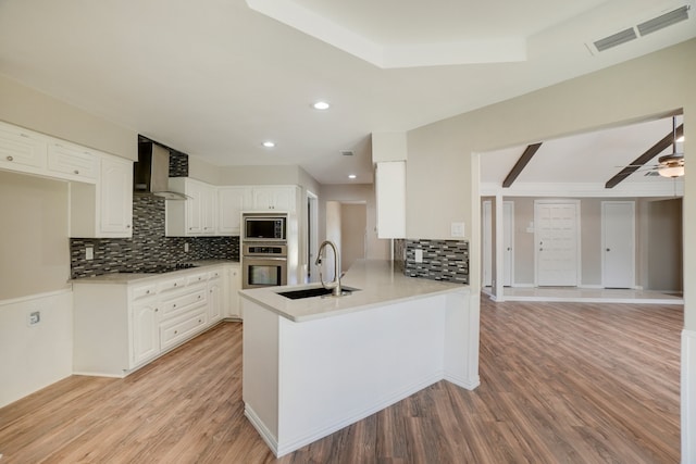 kitchen featuring kitchen peninsula, wall chimney range hood, sink, white cabinets, and light hardwood / wood-style floors