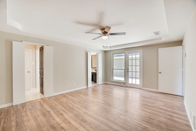 empty room with ceiling fan, light wood-type flooring, and a tray ceiling