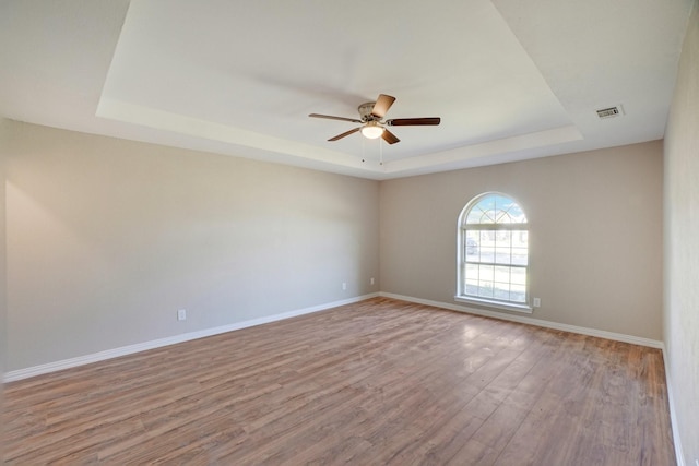 unfurnished room featuring a tray ceiling, light hardwood / wood-style floors, and ceiling fan