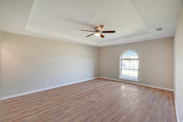 empty room with a raised ceiling, ceiling fan, and light wood-type flooring