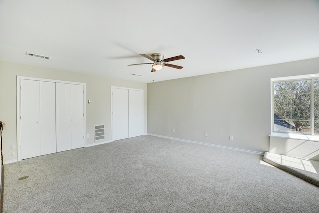 unfurnished bedroom featuring two closets, carpet floors, and ceiling fan