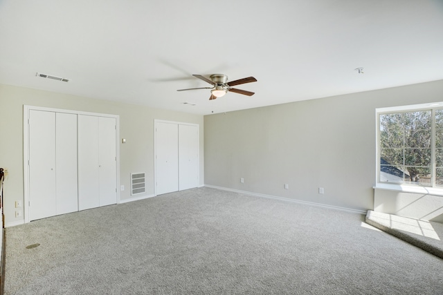 unfurnished bedroom featuring ceiling fan, carpet floors, and two closets