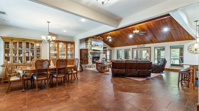 dining area with ceiling fan with notable chandelier, a fireplace, and vaulted ceiling with beams