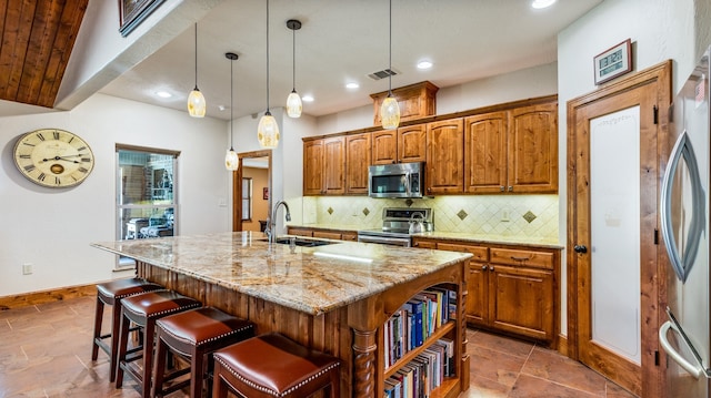 kitchen with stainless steel appliances, light stone counters, an island with sink, sink, and a breakfast bar area