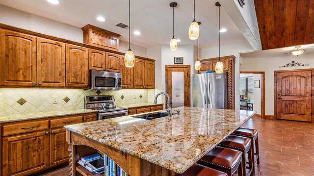 kitchen featuring decorative light fixtures, appliances with stainless steel finishes, light stone countertops, sink, and a center island with sink