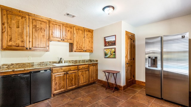 kitchen with light stone countertops, sink, stainless steel fridge, black dishwasher, and a textured ceiling