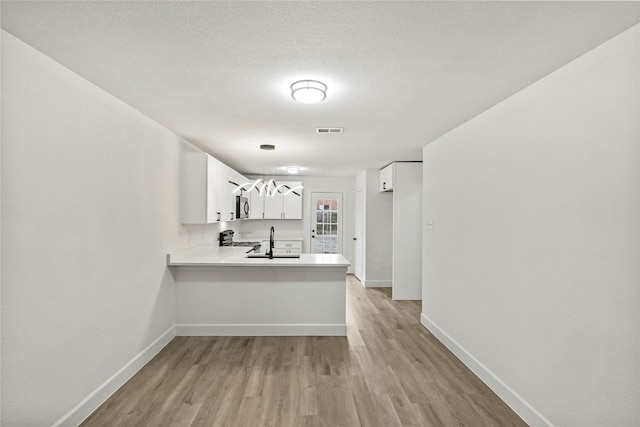 kitchen with white cabinetry, light hardwood / wood-style flooring, stainless steel appliances, kitchen peninsula, and sink