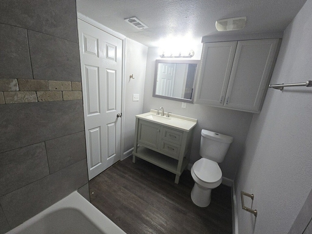 bathroom featuring a tub to relax in, vanity, a textured ceiling, hardwood / wood-style floors, and toilet