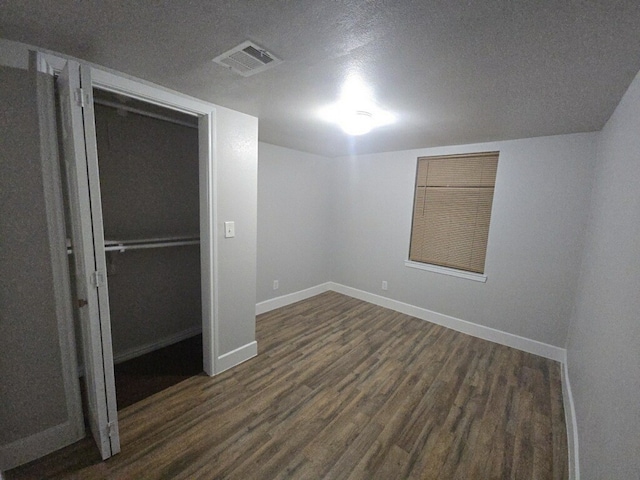 unfurnished bedroom featuring a textured ceiling, dark wood-type flooring, and a closet