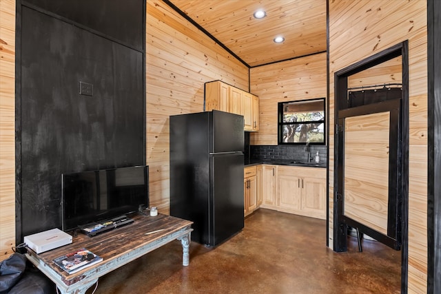 kitchen with wood walls, sink, light brown cabinets, lofted ceiling, and black fridge