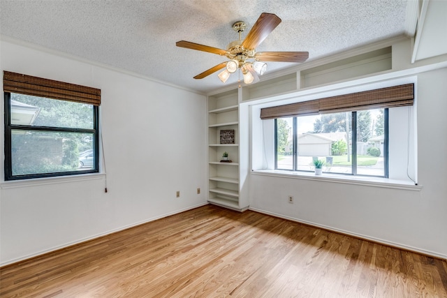 unfurnished room featuring light hardwood / wood-style flooring, ceiling fan, crown molding, a textured ceiling, and built in shelves